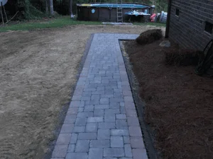 Gray and charcoal interlocking paver walkway with dark edging beside a mulched bed and brick wall