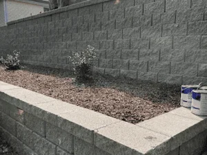 Gray split-face concrete block retaining wall with flat cap and mulched garden bed with small shrubs