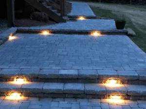 Gray interlocking pavers forming steps and a walkway with recessed warm LED step lights glowing at dusk
