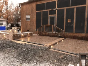 Stamped concrete patio in brick-paver pattern with stacked stone retaining wall and integrated step lights