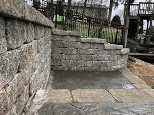 Stacked natural stone retaining wall with stepped cap and large flagstone paver patio below