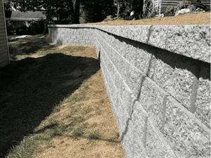 Gray split-face concrete retaining wall with staggered block courses and a level cap along a sloped lawn edge