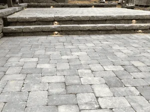 Gray interlocking concrete paver patio with stepped charcoal segmental block walls and steps