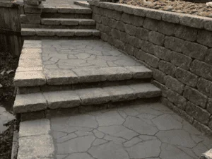 Gray segmental block retaining wall with stamped concrete stepped walkway and flagstone pattern