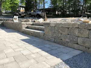 Stacked gray stone retaining wall beside light gray paver steps and walkway with gravel edging